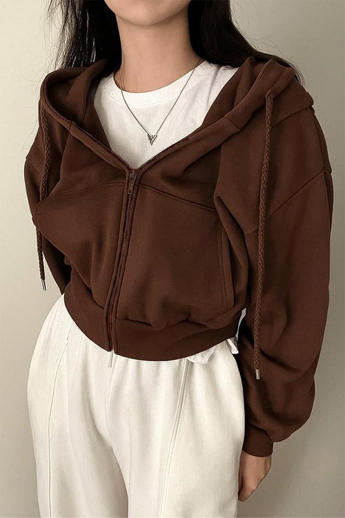 Person wearing a brown hoodie over a white shirt with a neutral background