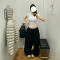 Person taking a mirror selfie wearing a white top and black pants in a fitting room.