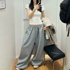 Person wearing a white top and gray sweatpants standing in front of a mirror.