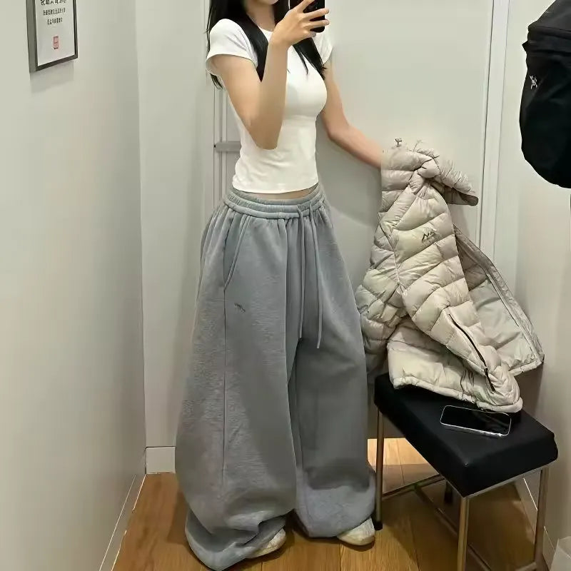Person wearing a white top and gray sweatpants standing in front of a mirror.