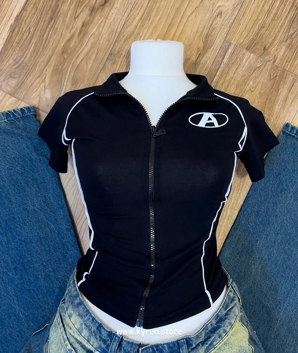Black zip-up shirt with a logo on a mannequin against a wooden floor background