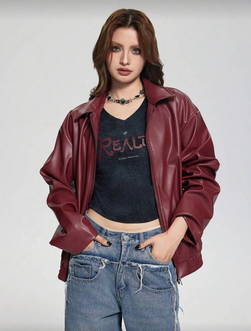 Person wearing a red leather jacket, black t-shirt with text, and blue jeans on a plain background