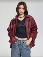 Person wearing a red leather jacket, black t-shirt with text, and blue jeans on a plain background