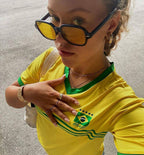 Person wearing a yellow Brazil soccer jersey with sunglasses and a neutral background