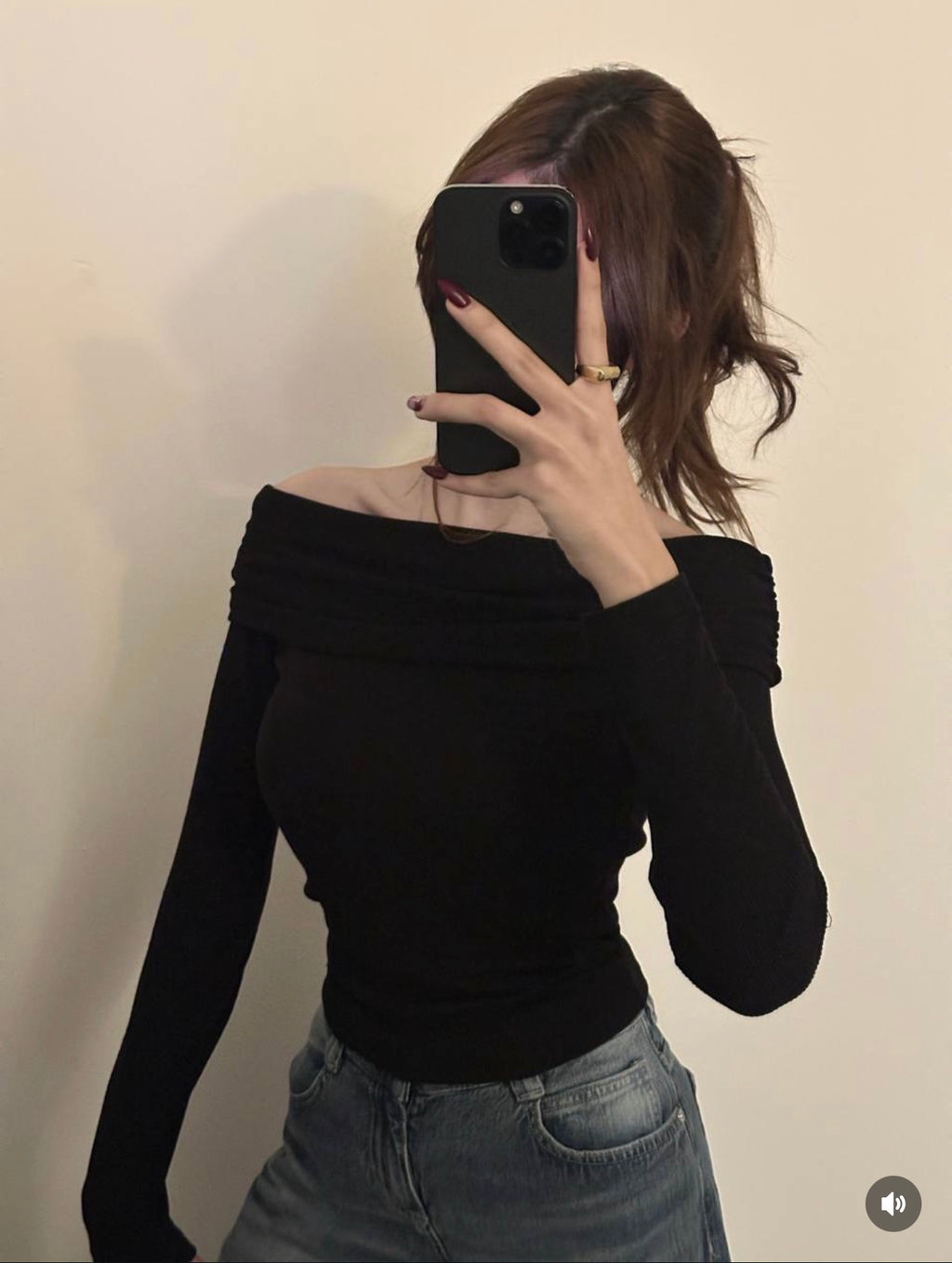 Person wearing a black off-shoulder top and jeans, taking a mirror selfie.