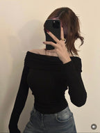 Person wearing a black off-shoulder top and jeans, taking a mirror selfie.