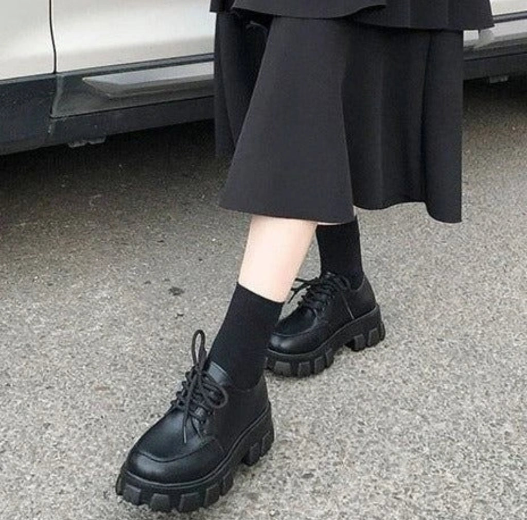 Person wearing black platform shoes and black pants on a pavement.
