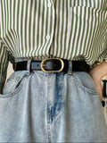 Person wearing a green and white striped shirt with a black belt and blue jeans.