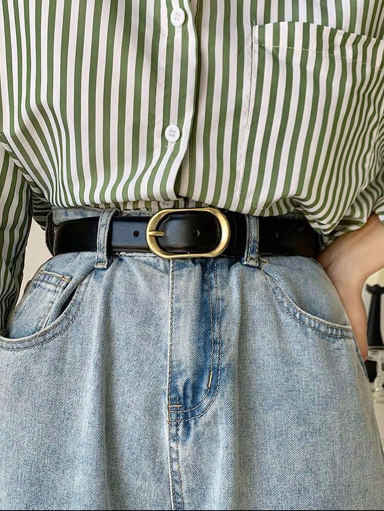 Person wearing a green and white striped shirt with a black belt and blue jeans.