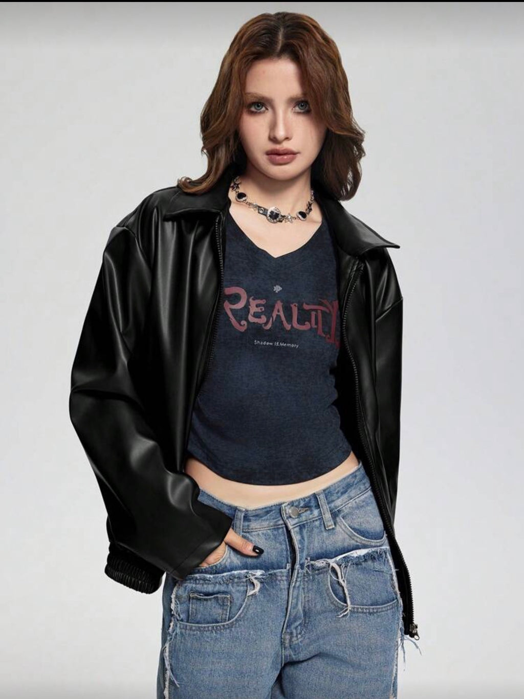 Person wearing a black leather jacket, dark blue t-shirt with 'REALITY' text, and blue jeans on a plain background