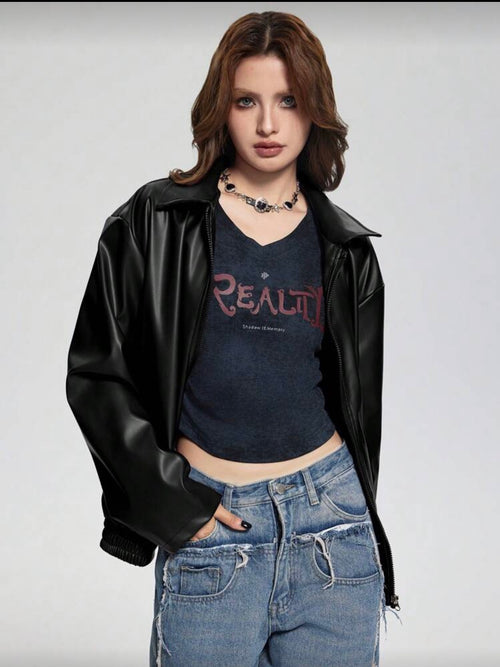 Person wearing a black leather jacket, dark blue t-shirt with 'REALITY' text, and blue jeans on a plain background