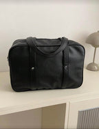 Black duffel bag on a white surface with a neutral background
