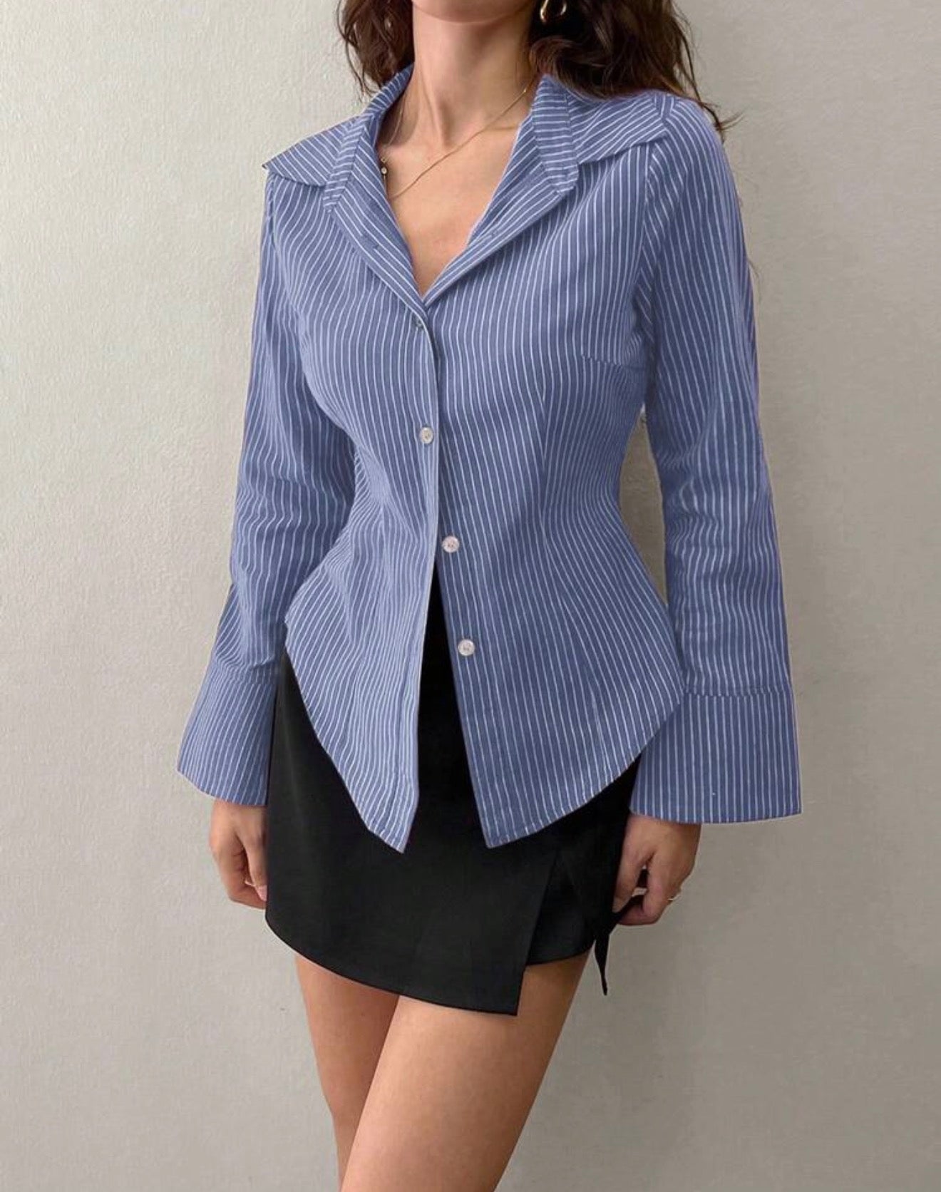 Person wearing a blue and white striped shirt over a black skirt against a plain background