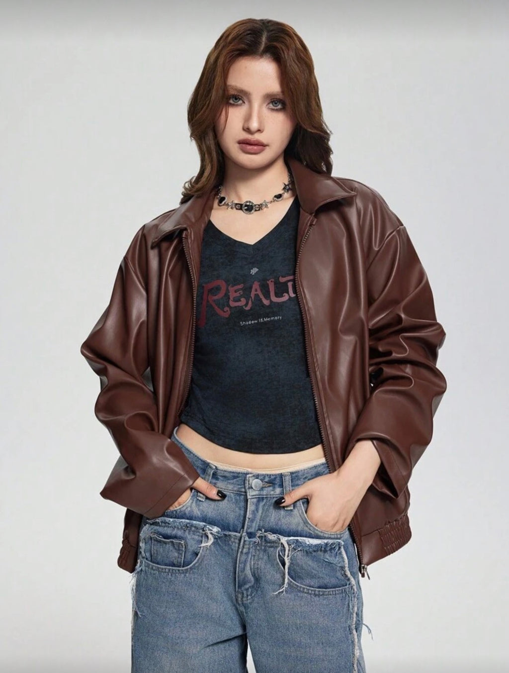 Person wearing a brown leather jacket, black t-shirt with text, and blue jeans on a plain background
