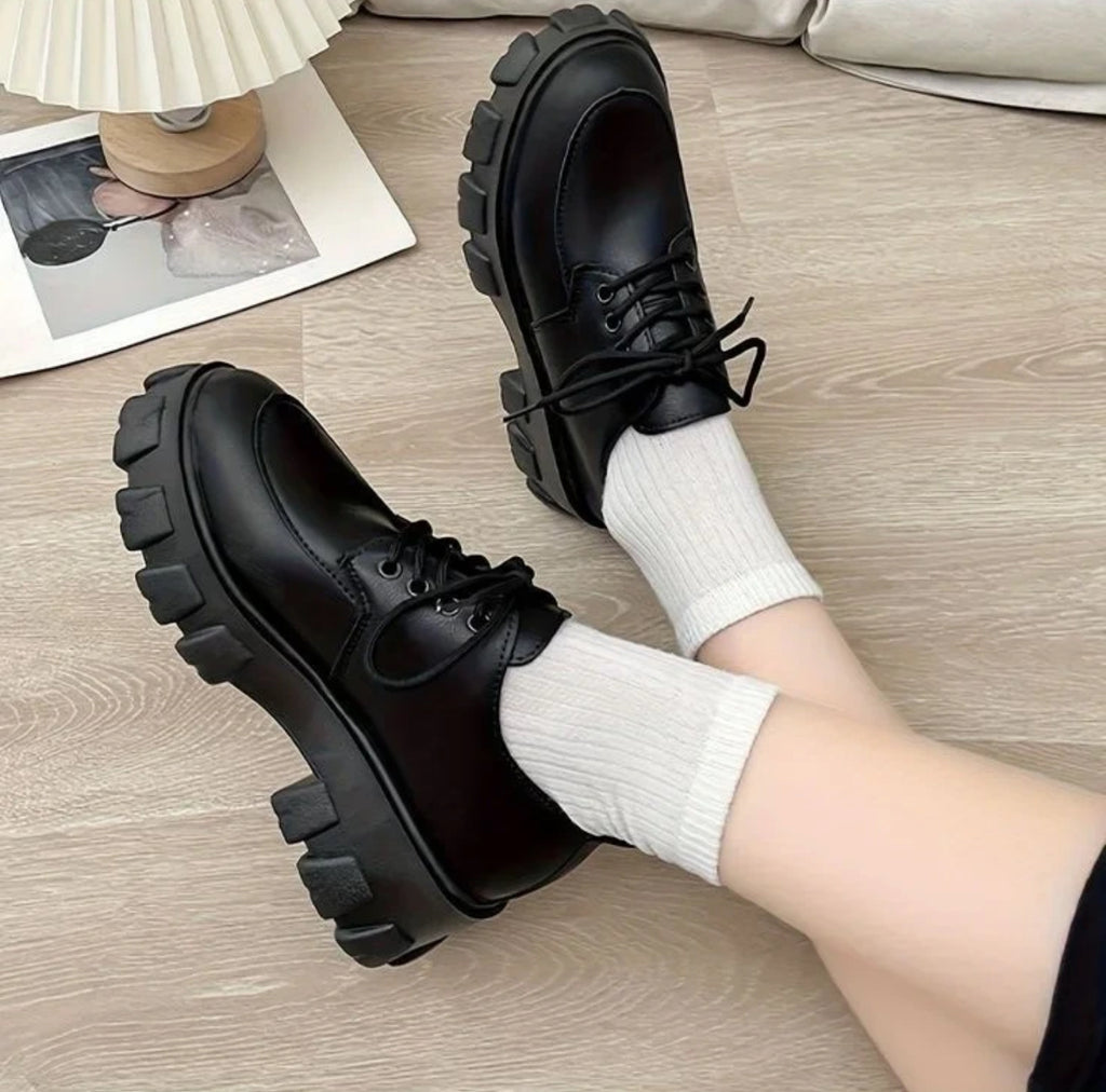 Black shoes with thick soles worn with white socks on a wooden floor.