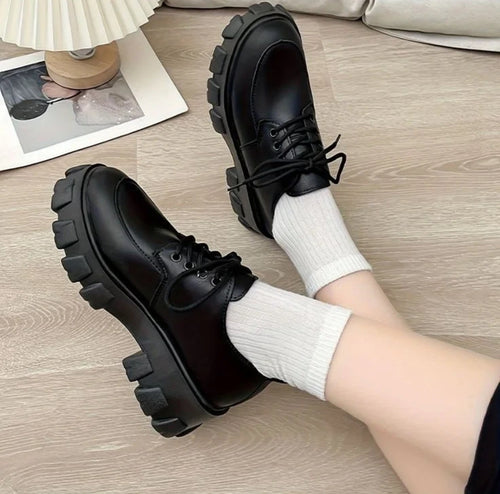 Black shoes with thick soles worn with white socks on a wooden floor.