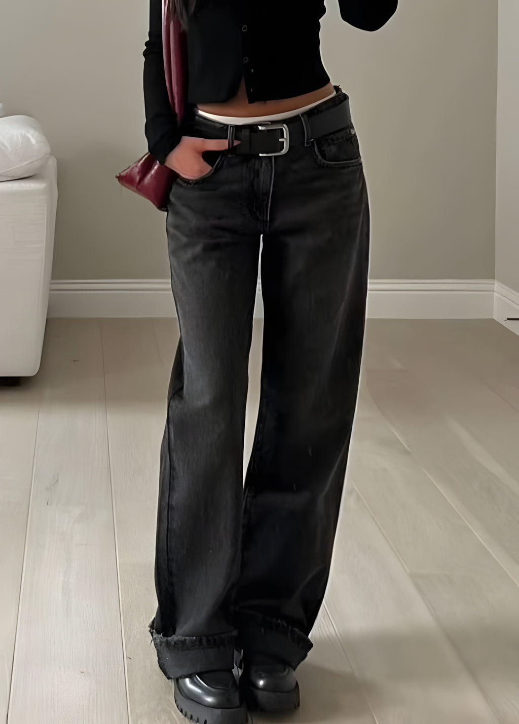 Person wearing black high-waisted jeans and black shoes in a minimal indoor setting.