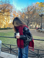 Person wearing a red scarf and black leather jacket in a park with autumn trees.