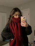 Person wearing a red scarf and taking a mirror selfie with a phone.