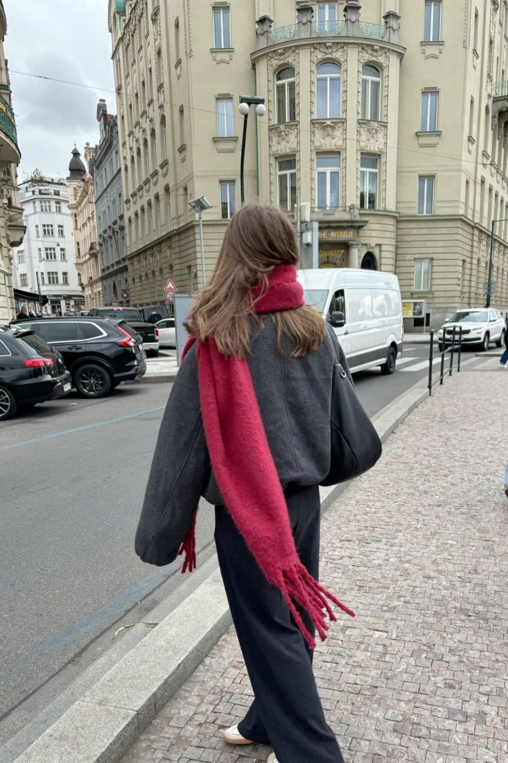 Person walking on a city street with a red scarf and black coat
