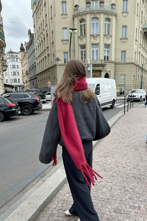 Person walking on a city street with a red scarf and black coat