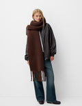 Person wearing a long brown scarf, black jacket, and jeans on a white background
