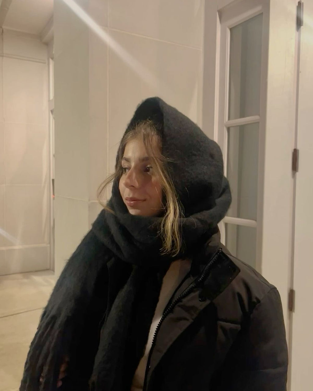 Person wearing a dark coat and scarf in an indoor setting