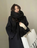 Person wearing a black scarf and coat with a neutral background