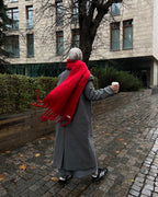 Person wearing a red scarf and gray coat walking on a sidewalk with a building in the background.
