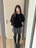 Person taking a mirror selfie wearing a black coat, gray pleated skirt, and black boots.