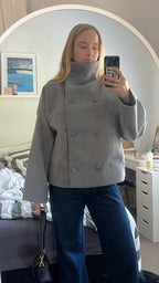 Person wearing a gray coat taking a mirror selfie in a bedroom.