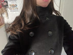 Person wearing a black coat with visible buttons indoors.