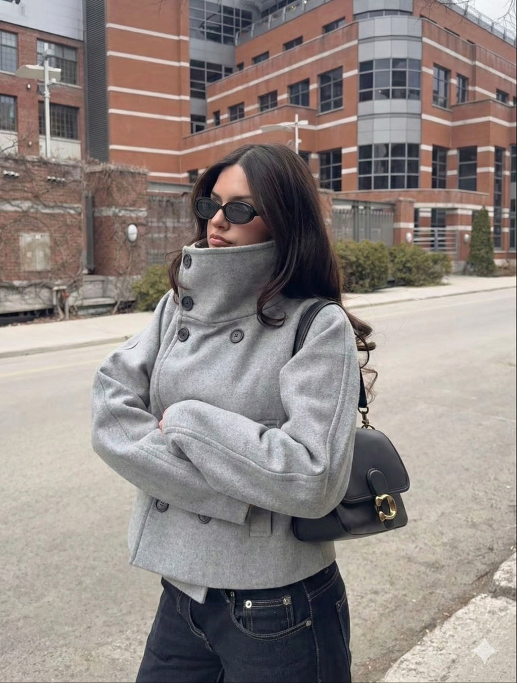 Person wearing a gray coat and sunglasses in an urban setting