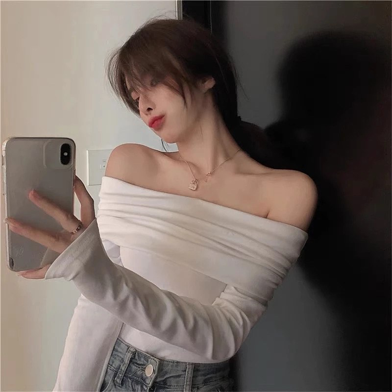 Woman taking a mirror selfie wearing a white off-shoulder top and denim shorts.