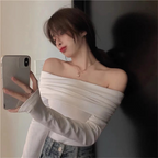 Woman taking a mirror selfie wearing a white off-shoulder top and denim shorts.