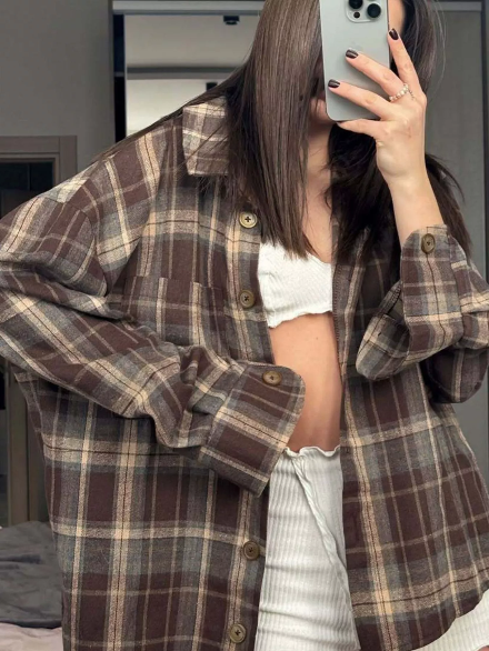 Person wearing a plaid shirt over a white top, taking a mirror selfie.