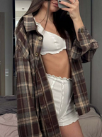 Person wearing a plaid shirt over a white top and shorts, taking a mirror selfie.