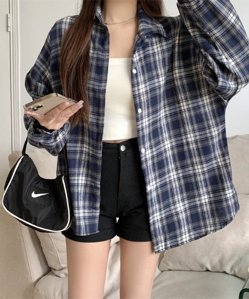Person wearing a blue and white plaid shirt with black shorts, holding a phone and a Nike bag.