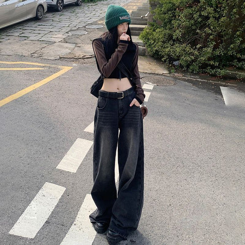 Person wearing a green beanie, brown long-sleeve top, and black wide-leg jeans standing on a street.