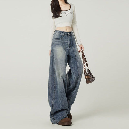 Person wearing a white crop top and blue jeans holding a brown bag on a plain background