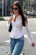 Woman in a white shirt and blue jeans walking on a city street.