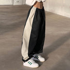 Person wearing black and beige pants with white sneakers on a concrete floor.
