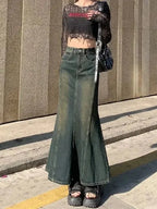 Person wearing a black lace top and green wide-leg jeans standing on a sidewalk.