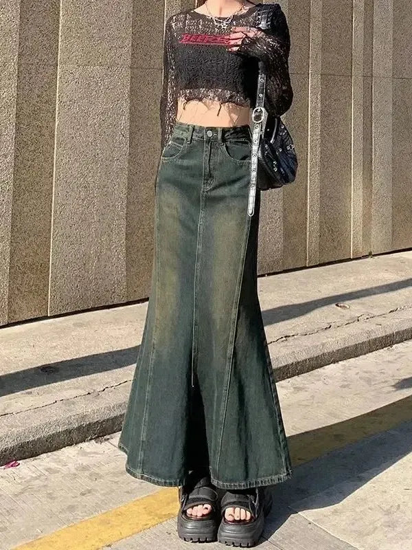 Person wearing a black lace top and green wide-leg jeans standing on a sidewalk.