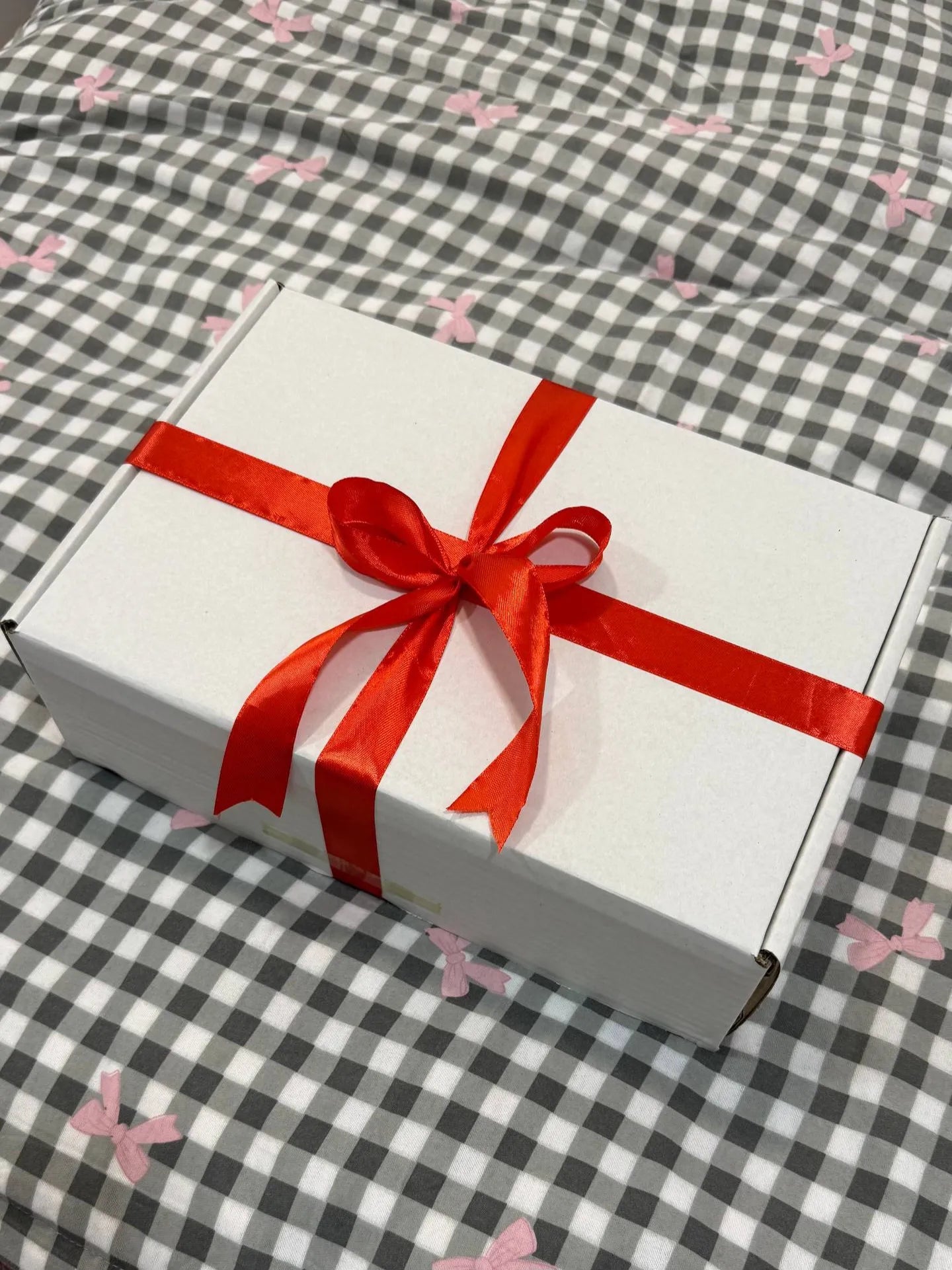 White gift box with a red ribbon on a checkered fabric background