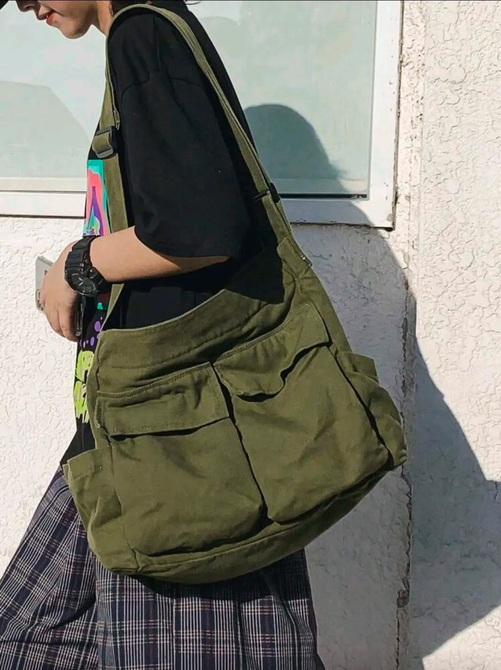 Person wearing a green shoulder bag against a light-colored wall.