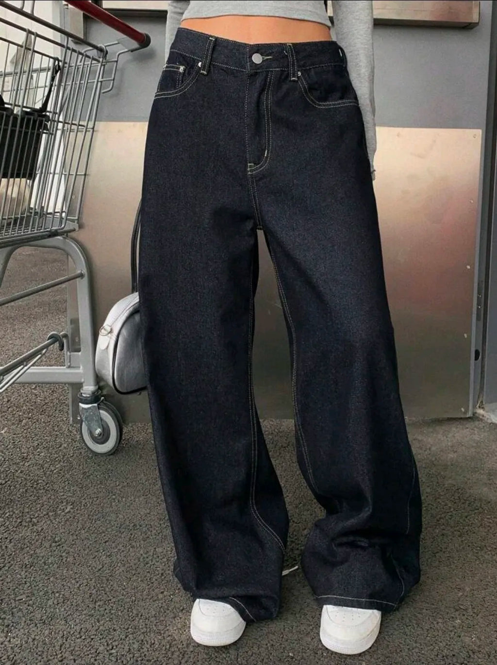 Person wearing black wide-leg jeans standing in a parking lot.