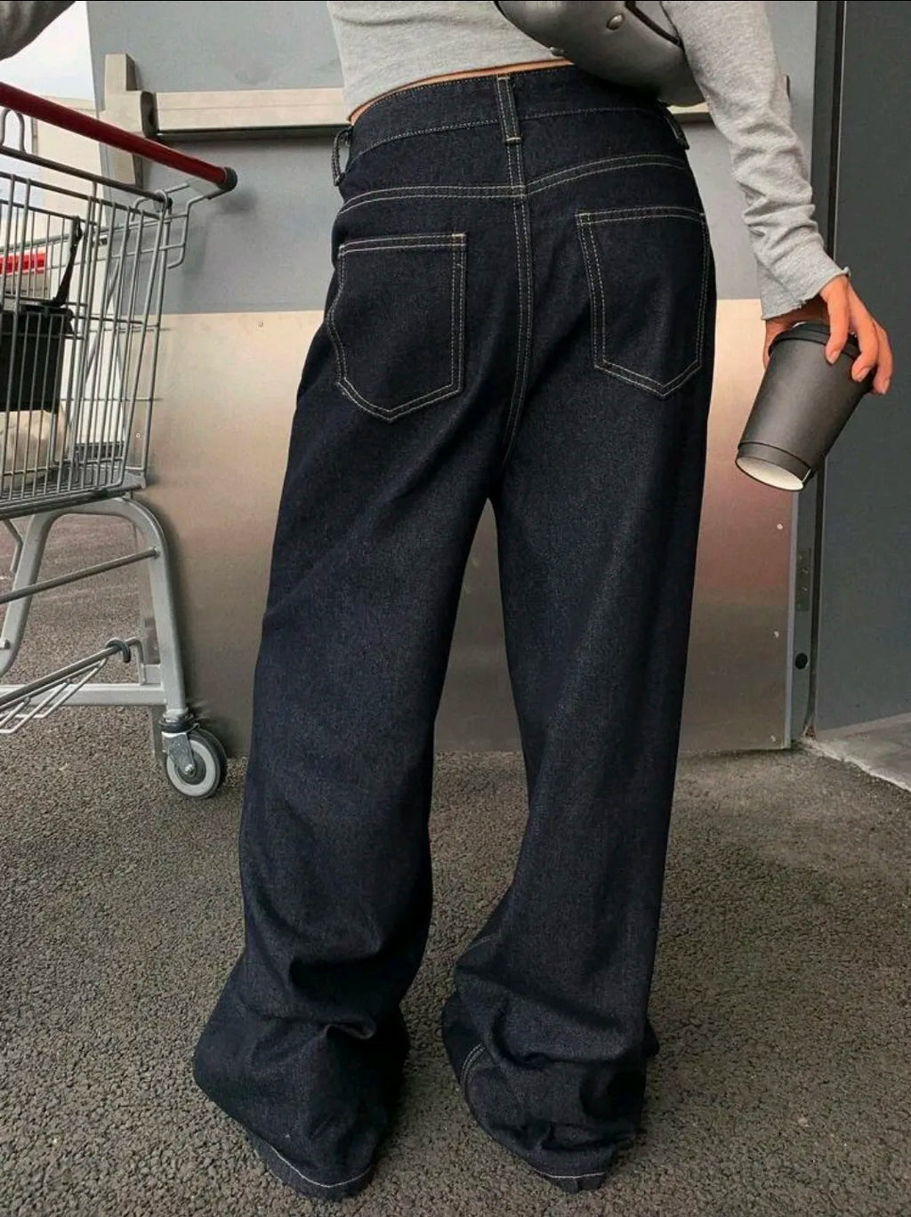 Person wearing dark blue jeans holding a cup in an indoor setting.