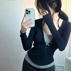 Person wearing a black cardigan over a gray top, holding a phone.