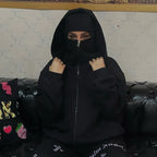 Person wearing a black hoodie sitting on a couch with a patterned wall in the background